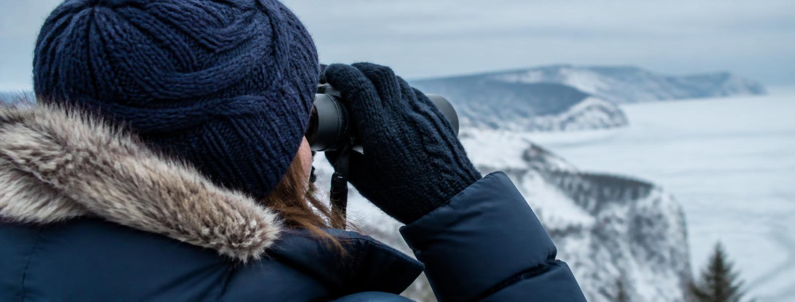 Ornithologue avec jumelles regardant un paysage hivernal gaspésien